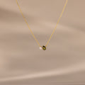 The Teardrop Peridot & Pearl Necklace, featuring a small green peridot and a white pearl pendant, rests on a soft beige background—a timeless gift for any occasion.