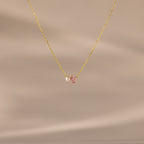 The Teardrop Pink Tourmaline & Pearl Necklace features a delicate gold teardrop pendant with a pink gemstone and pearl, set against a soft beige background—a timeless gift for any occasion.