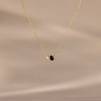 The Teardrop Onyx & Pearl Necklace features a gold chain with a delicate white pearl and black teardrop onyx pendant, displayed on a neutral beige background—an elegant, timeless gift for any occasion.