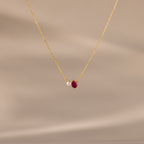 The Teardrop Ruby & Pearl Necklace showcases a delicate pearl and red teardrop birthstone pendant on a soft beige backdrop—perfect for celebrating milestones.