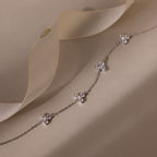 Delicate silver bracelet with floral pendants on a soft beige fabric background
