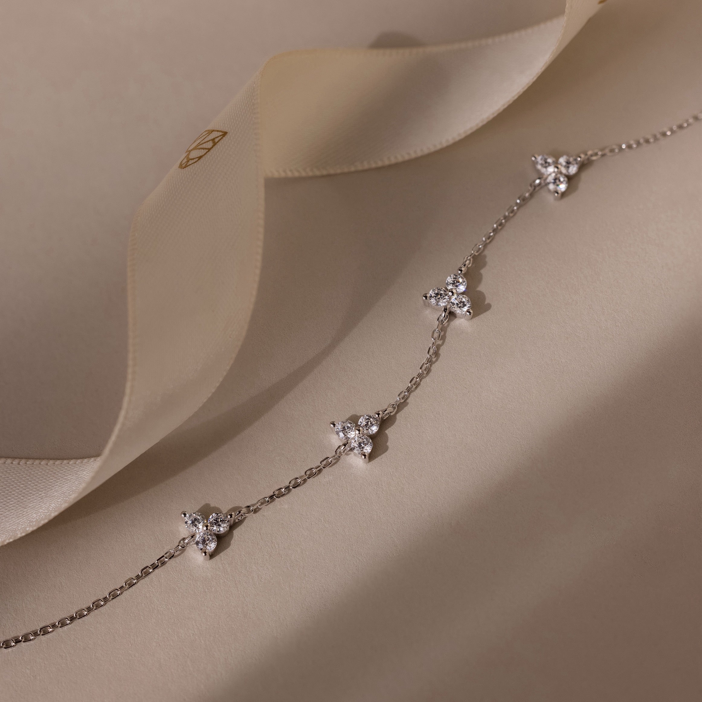 Delicate silver bracelet with floral pendants on a soft beige fabric background