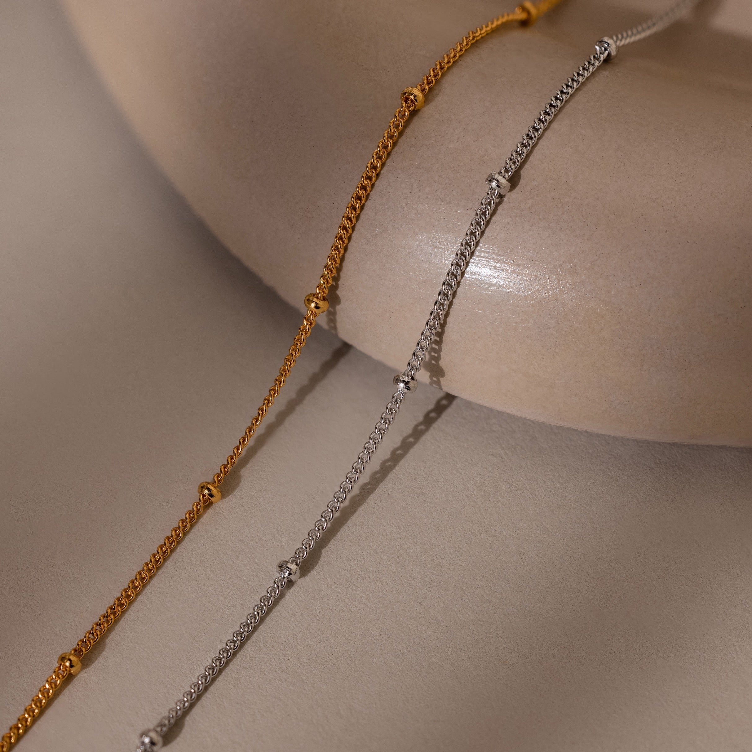 Two gold and silver beaded bracelets on a beige surface
