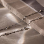 Silver double chain anklet with beads on a textured surface