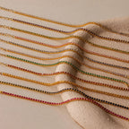 The Classic Birthstone Tennis Bracelet is arranged in a parallel line with other gold chain gemstone bracelets on a textured beige surface.