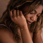 A woman with wavy hair gazes downward, wearing the Heart Station Bracelet. The delicate piece adds a romantic and graceful touch to her style.