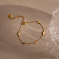 The Heart Station Bracelet features small heart charms and is shown on a textured beige surface—a romantic piece, perfect for stacking.