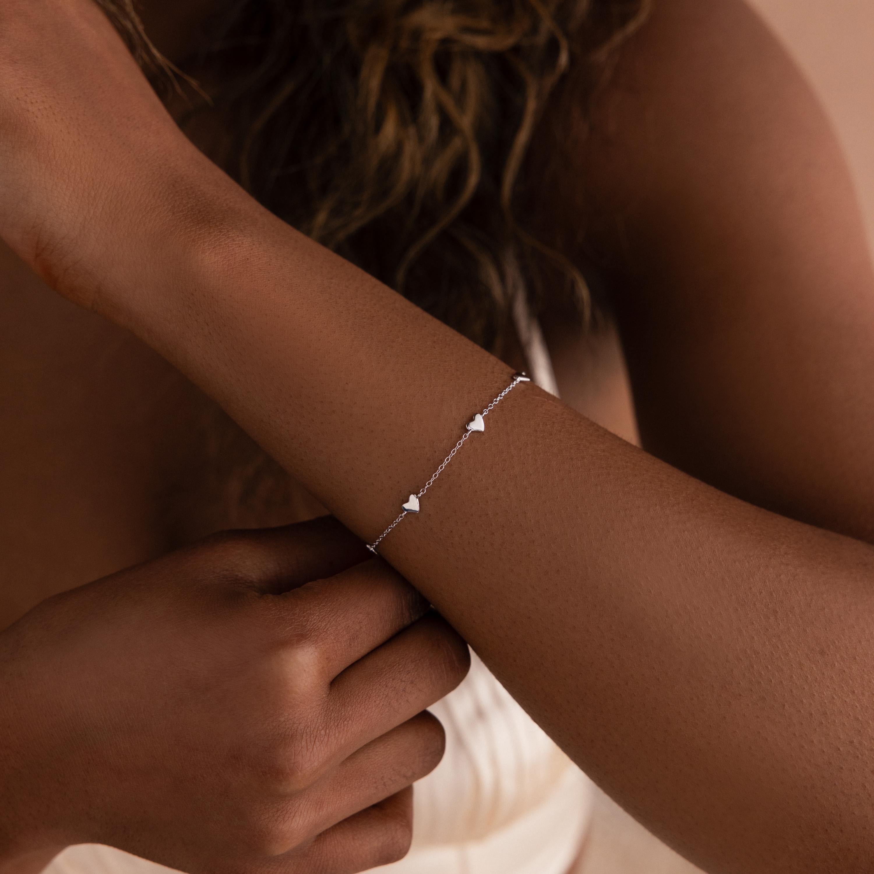 A woman wears the Heart Station Bracelet in Sterling Silver, featuring delicate heart charms on her wrist—a romantic touch that's perfect for stacking with other favorite jewelry pieces.