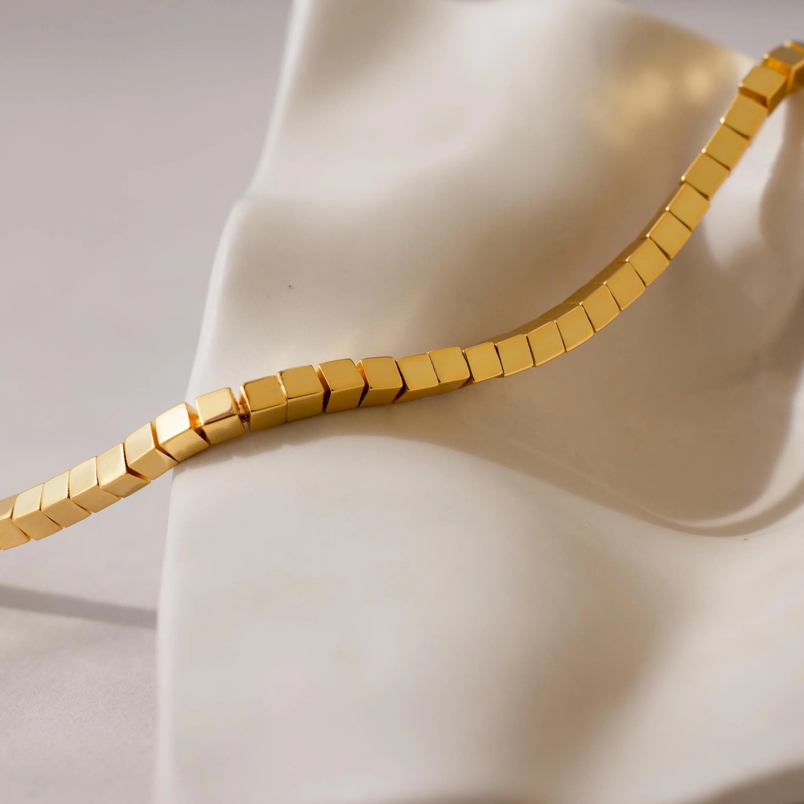 Cube Bracelet featuring geometric bead links, displayed on a smooth white sculptural surface—an elegant men's statement jewelry piece.