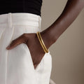 A person wearing white pants has their hand in their pocket, showcasing the Thick Snake Chain Bangle with a textured design.