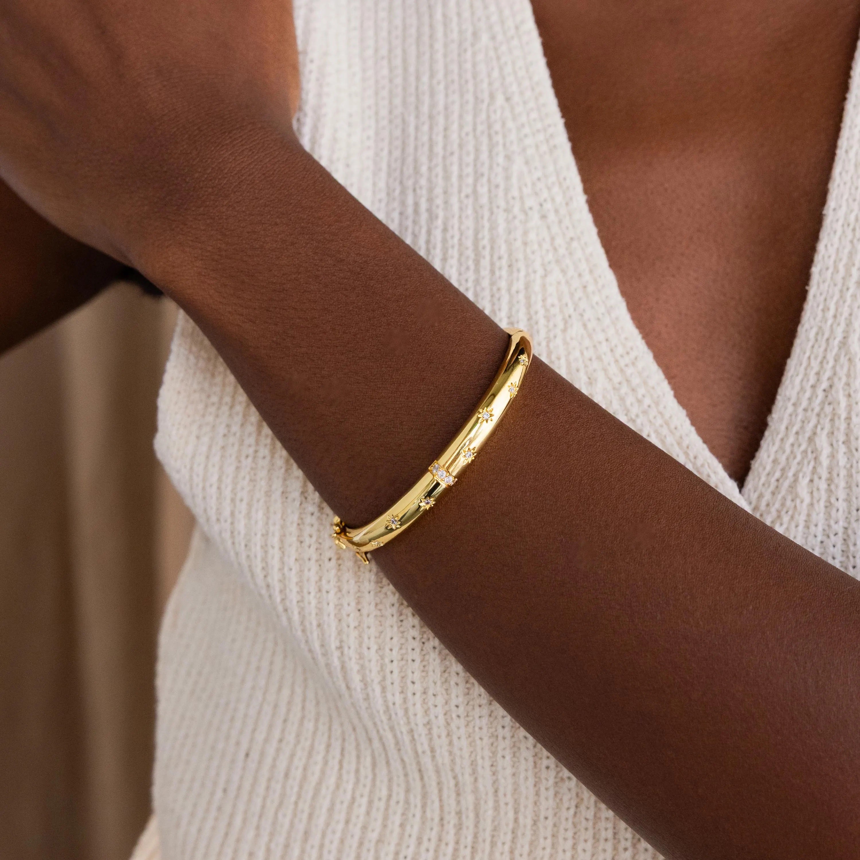Gold North Star Diamond Bangle on women's wrist. The bangle is a dome shaped and features multiple North Star with Diamond CZ designs dotted around the bangle