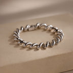 A Twisted Chain Bracelet with bold, gleaming links is displayed on a beige rectangular surface, exuding effortless glamour.