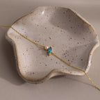 The Marquise Blue Zircon & Pearl Bracelet, featuring a blue gem and pearl, is displayed on a speckled wavy ceramic dish—a perfect gift for someone special.