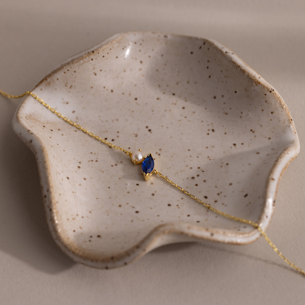 The Marquise Sapphire & Pearl Bracelet, displayed on a speckled ceramic dish, makes a perfect gift for someone special.