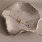 The Marquise Topaz & Pearl Bracelet features a gold chain, pearl accents, and a gold leaf charm—an elegant gift inspired by the timeless beauty of marquise birthstones. Displayed on a speckled ceramic dish.