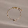 The Marquise Opal & Pearl Bracelet features two small gemstones and a heart charm, shown on a light beige background. A delicate gold bracelet—perfect as a gift for someone special.