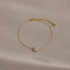 The Marquise Opal & Pearl Bracelet features two small gemstones and a heart charm, shown on a light beige background. A delicate gold bracelet—perfect as a gift for someone special.