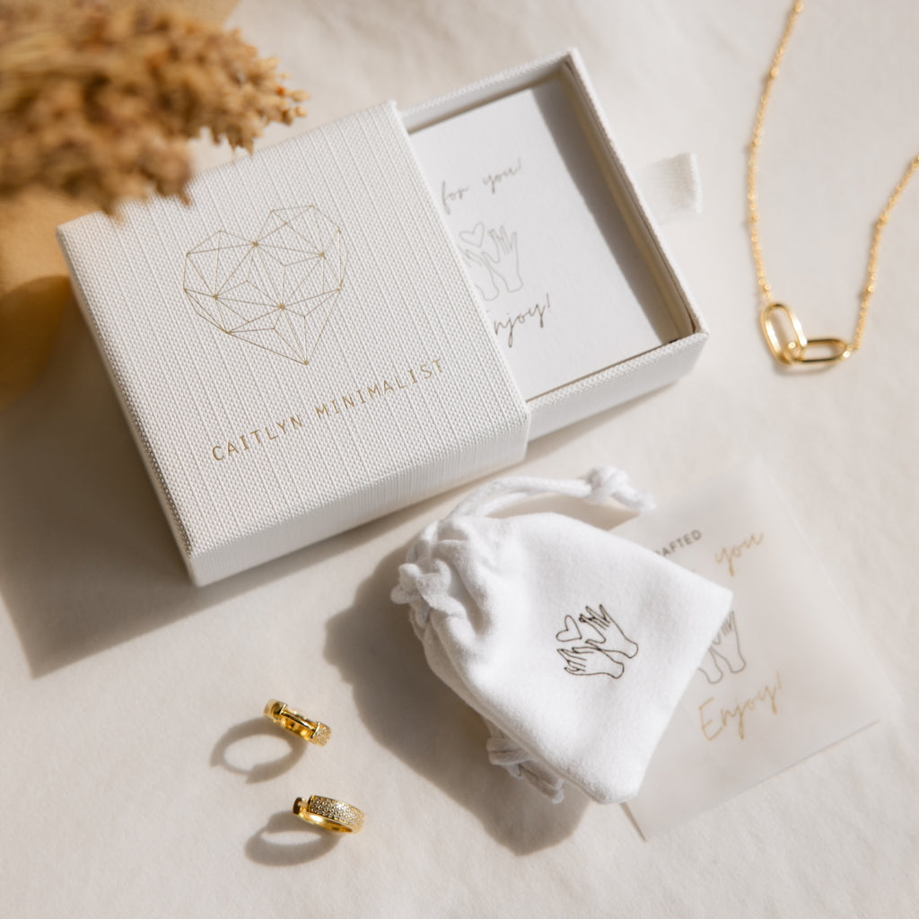 Minimalist jewelry set with gold rings, necklace, gift box, and white pouch on a light surface. Ships fast with U.S. FEDEX 2 Business Day Shipping for quick delivery and effortless style.