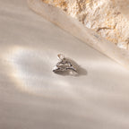 A close up of a silver Heart Hands charm placed on a light surface beside a stone.
