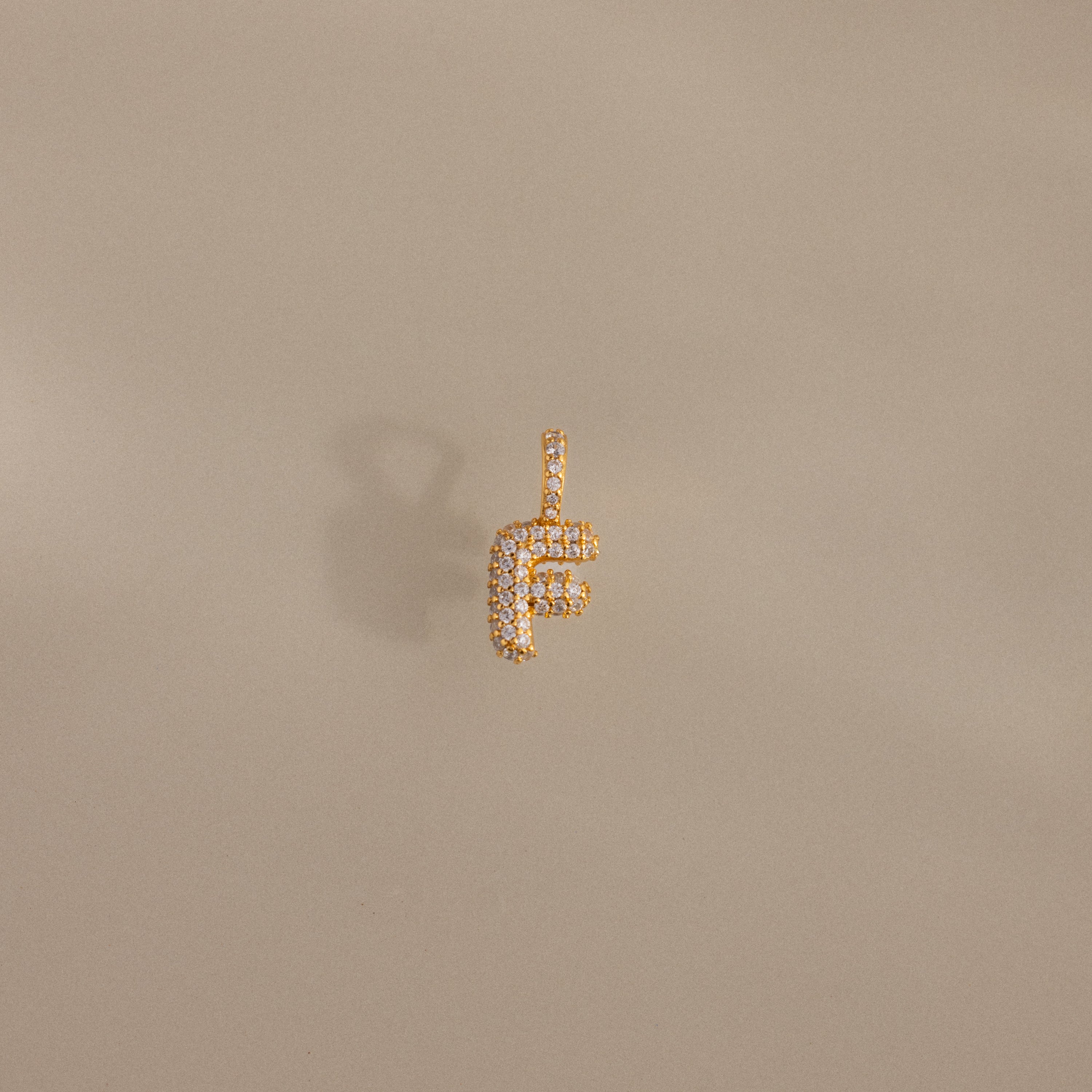 The Pave Bubble Letter Charm, shaped like the letter F with diamond-studded lettering, is shown against a beige background.
