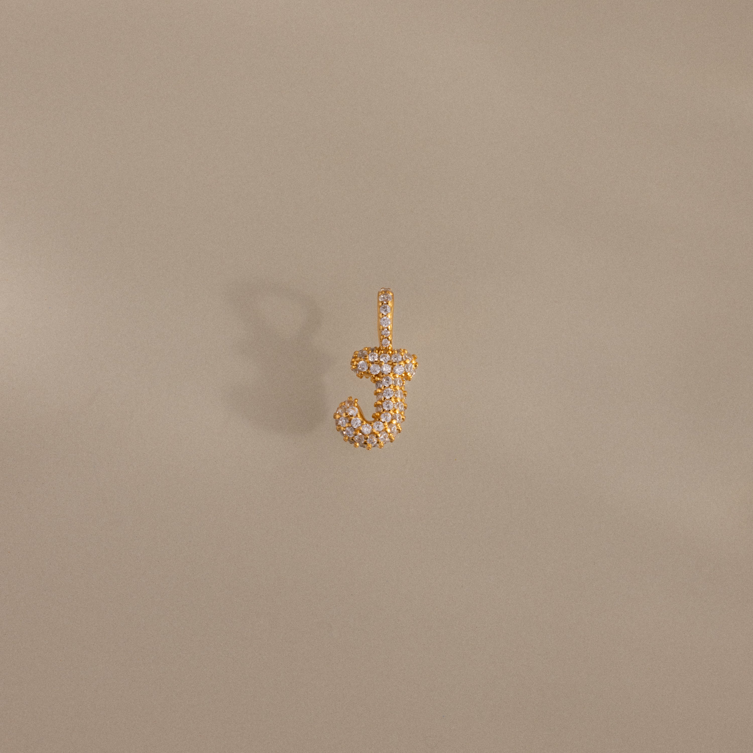 The Pave Bubble Letter Charm, a diamond-studded gold charm in the shape of the letter J, is showcased on a beige background.