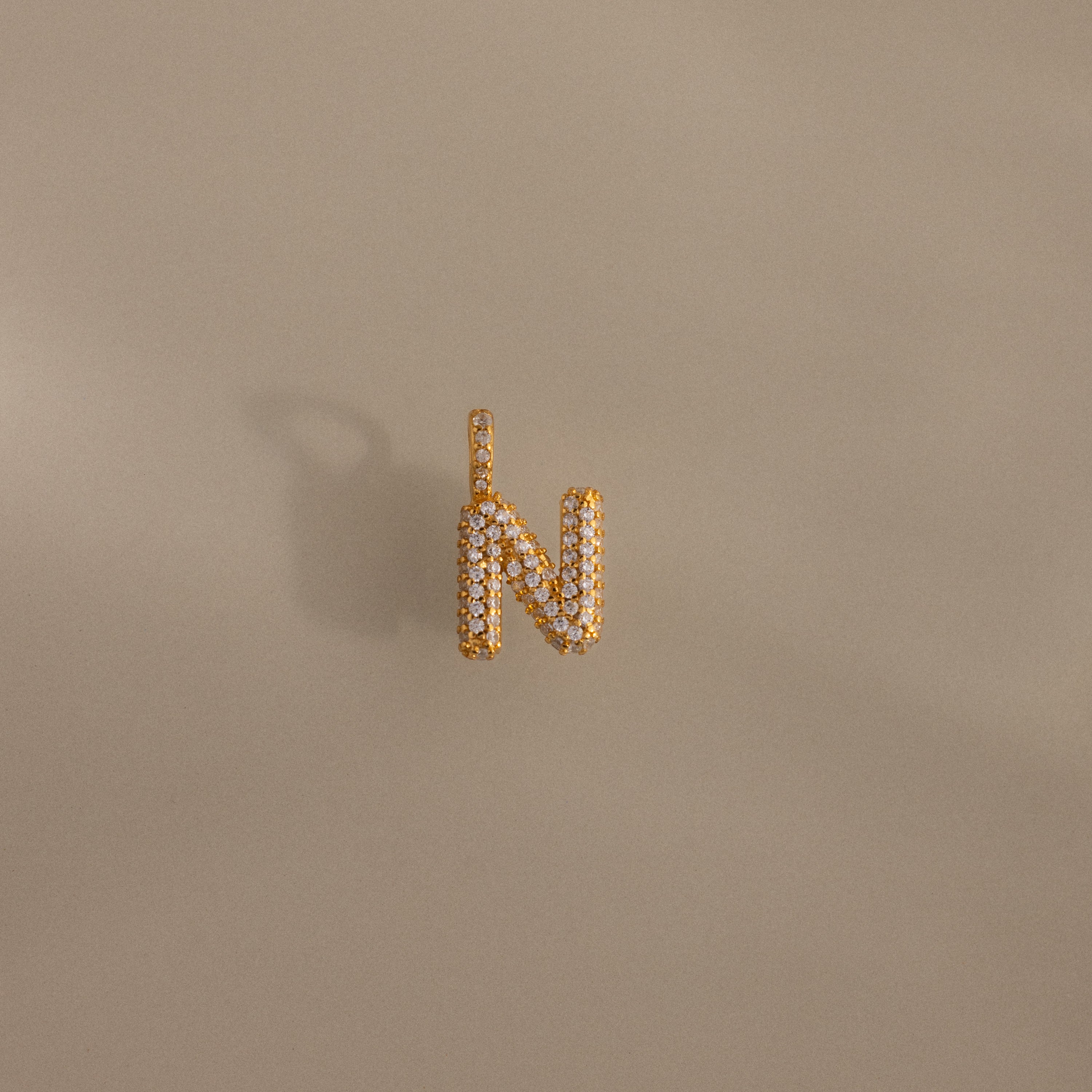 The Pave Bubble Letter Charm, shaped like the letter N with diamond-studded details, is displayed on a beige background.