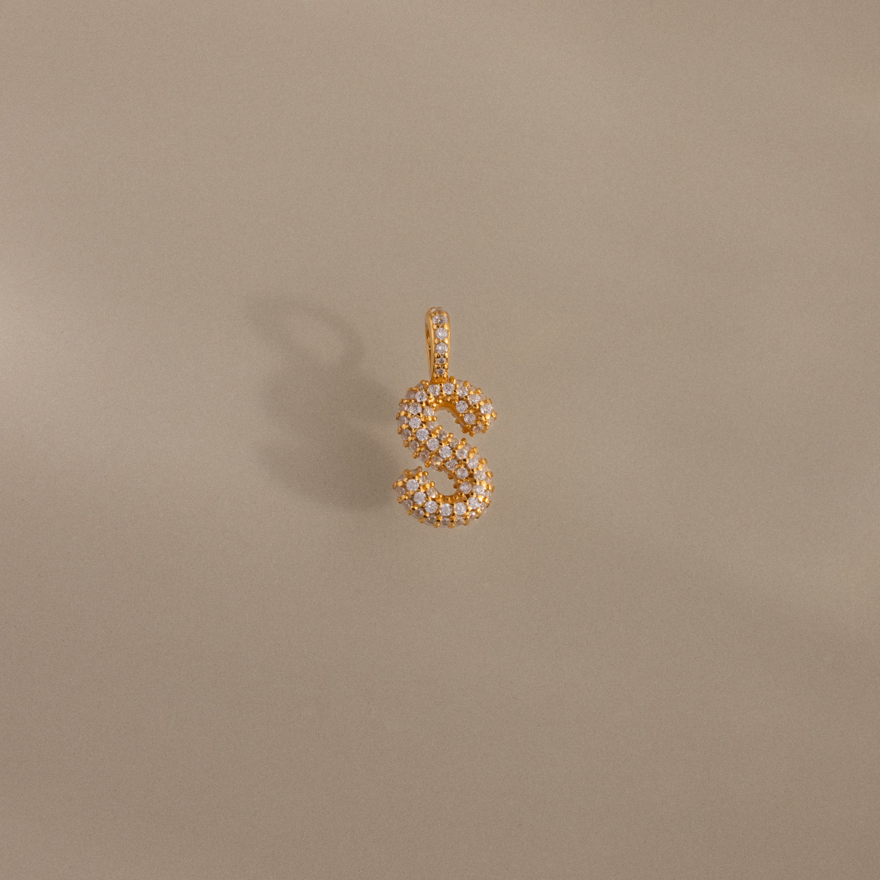 The Pave Bubble Letter Charm features gold and diamond-studded "S" lettering in a bubble style, shown on a beige background.