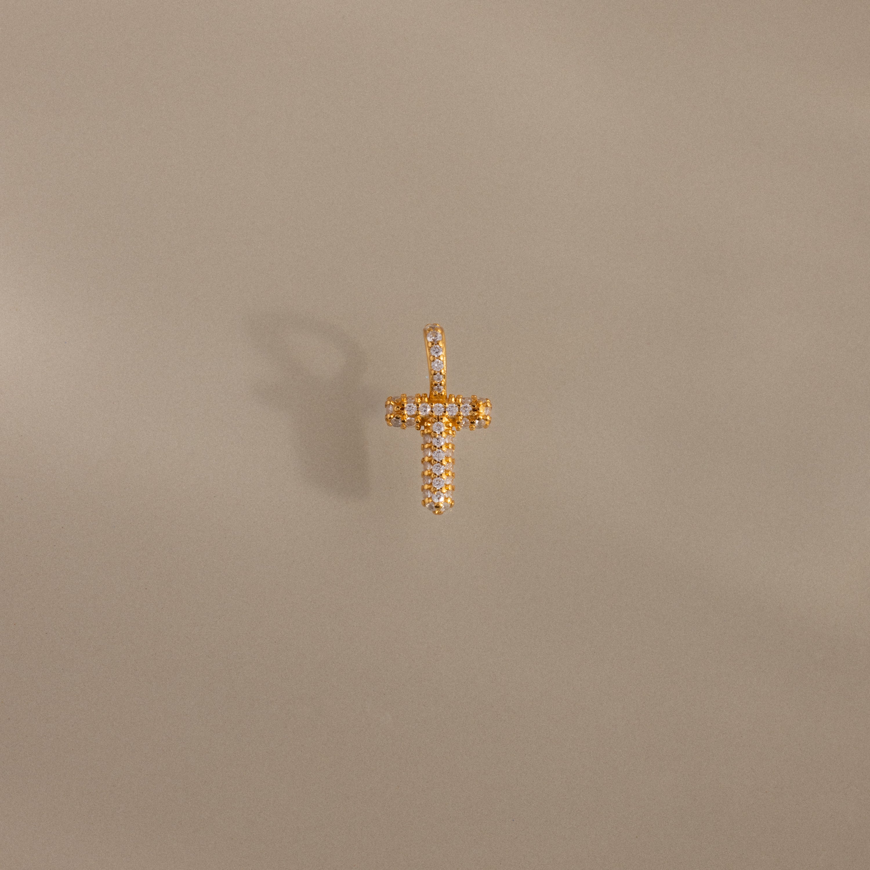 Gold cross pendant with small diamonds on a plain beige background, casting a faint shadow—pairs beautifully with the Pave Bubble Letter Charm or any elegant gold charm.