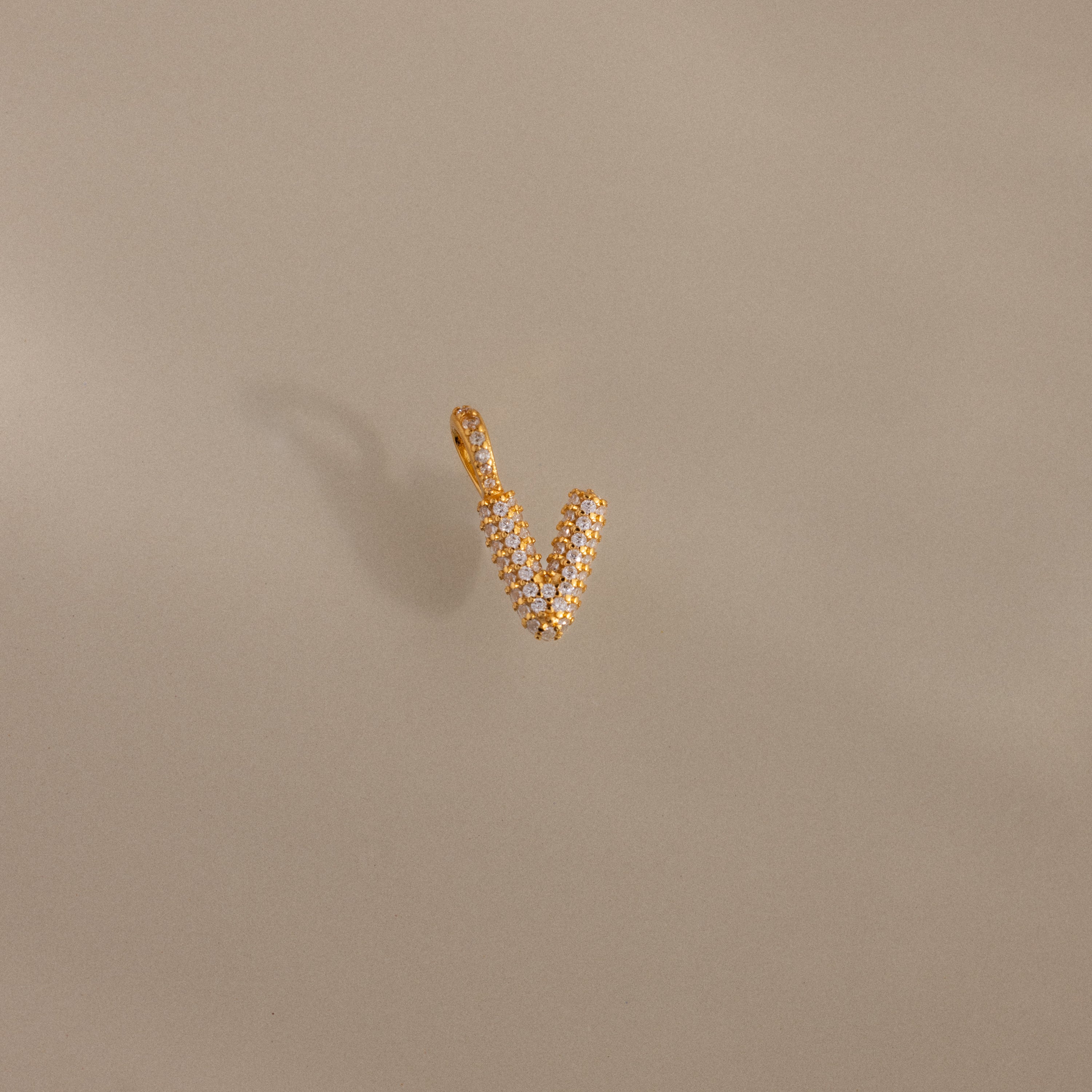 The Pave Bubble Letter Charm features diamond-studded V-shaped lettering with delicate pave details, shown on a beige background.