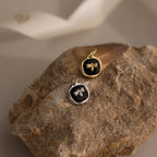 The Onyx Honeybee Charm, shown in both gold and silver on a textured rock with a neutral backdrop, brings nature-inspired charm to any jewelry collection.