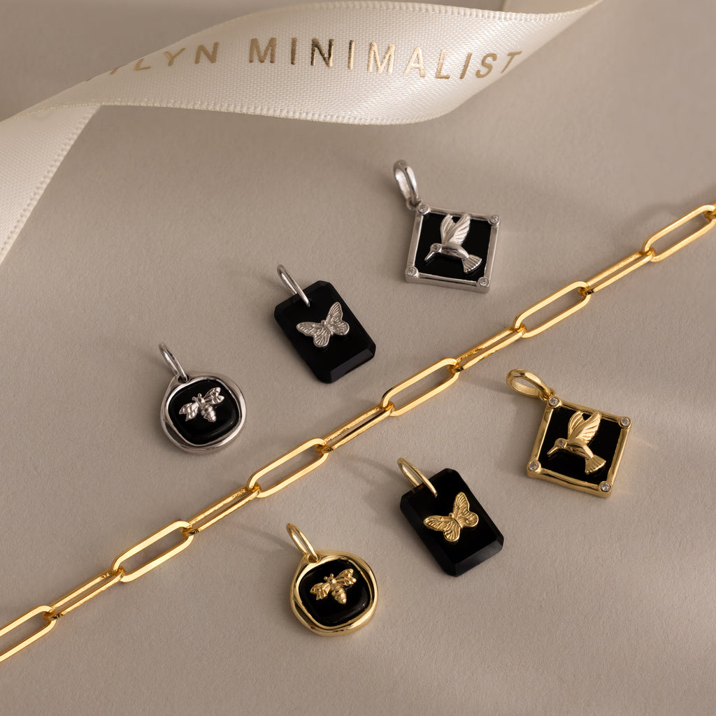 The Onyx Honeybee Charm in Silver dangles elegantly from a delicate chain bracelet, beautifully showcased on a neutral background for a refined product description.