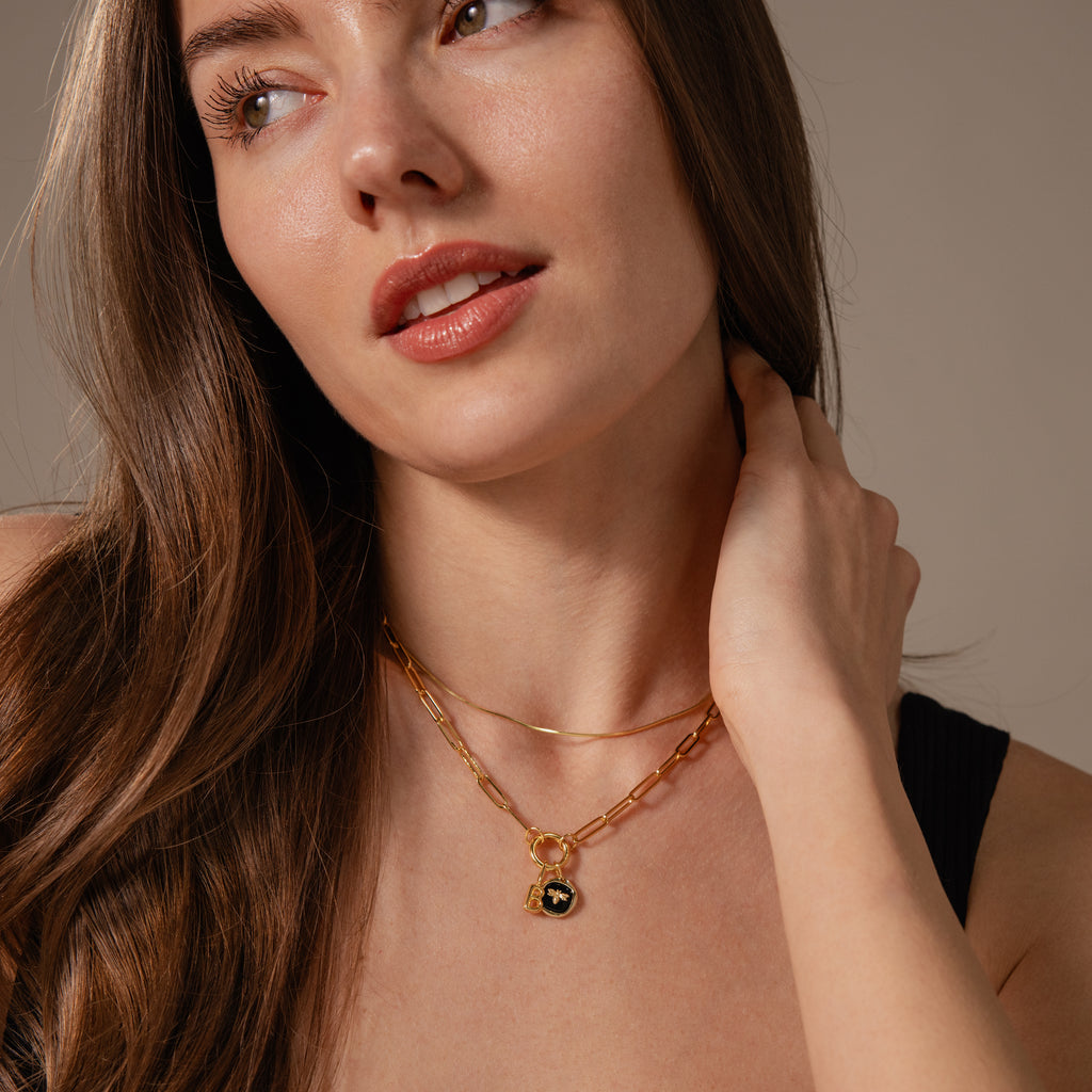Woman with long brown hair wearing an 18K gold Onyx Honeybee Charm necklace layered over a black top, looking slightly to the side. Perfect for adding elegance and unique style to any outfit.