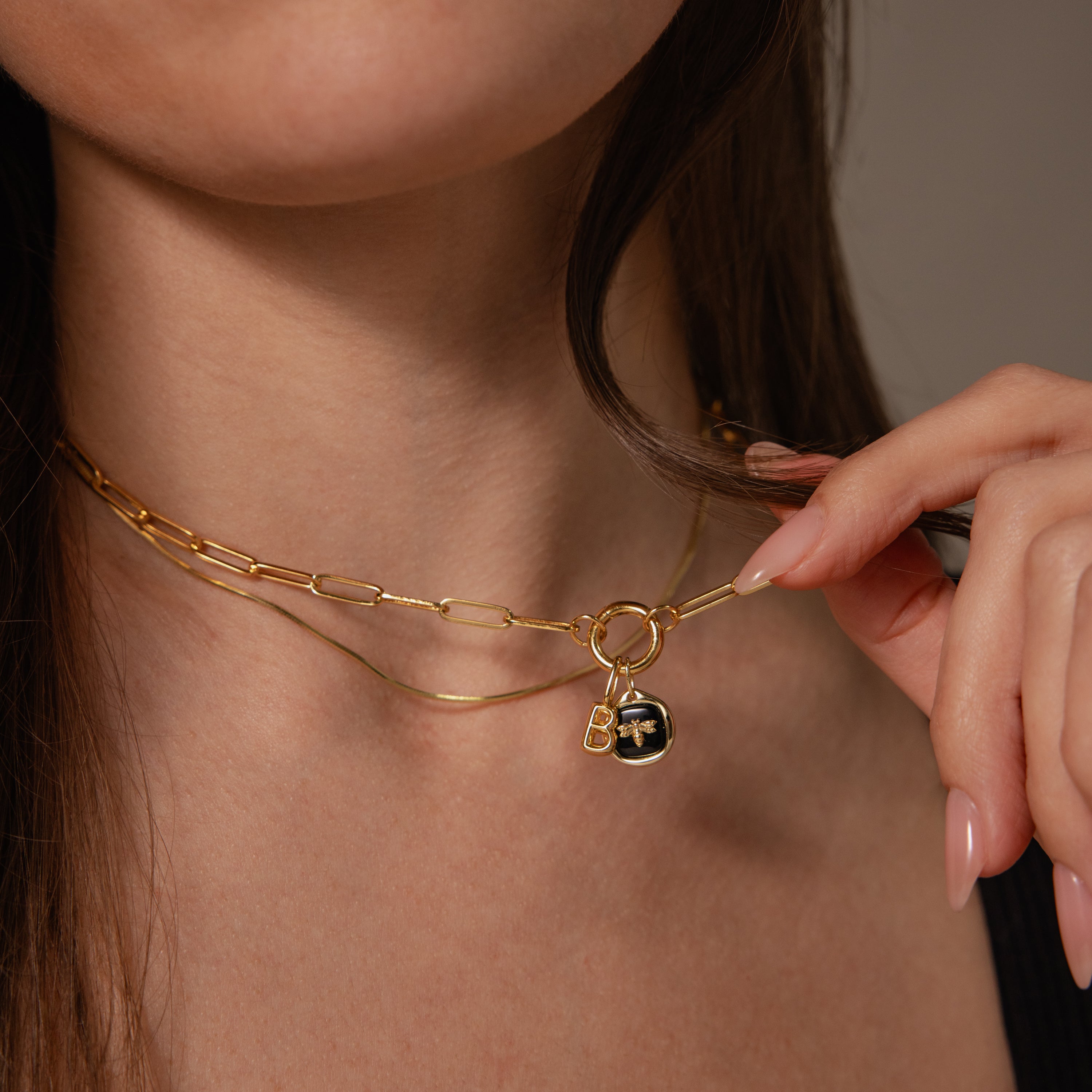 Close-up of a woman wearing layered necklaces, featuring the Onyx Honeybee Charm in Silver—an elegant silver pendant with a bee motif, perfect for adding unique style and shimmer to any outfit.