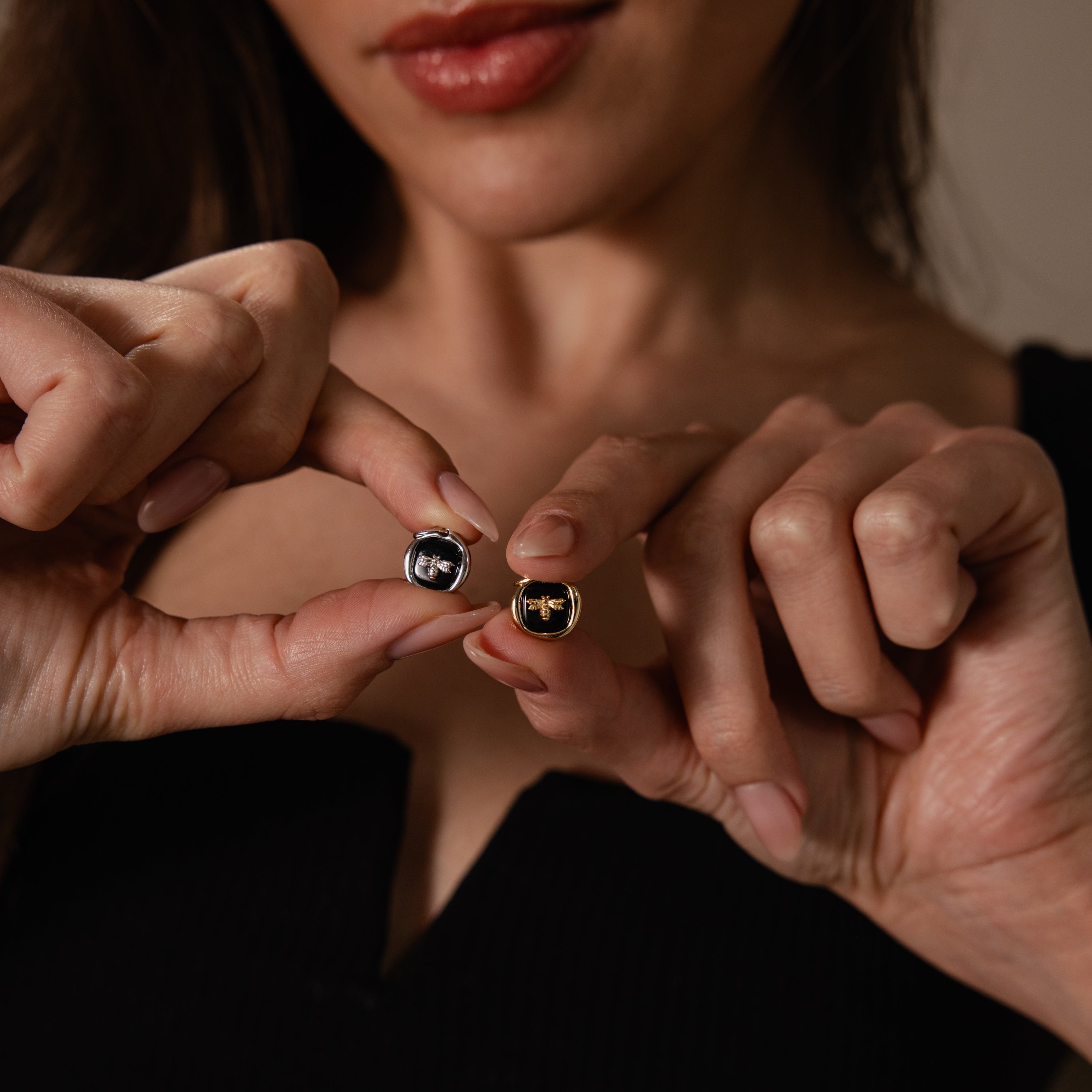 A woman holds an Onyx Honeybee Charm close to the camera—perfect for adding a touch of elegance to your style.