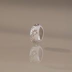 The Sprinkle Diamond Dome Charm in Silver stands upright on a reflective surface, its starburst-set stones and star-shaped engravings shining against a soft beige background.