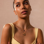 A woman in a yellow top wears layered gold necklaces, featuring the Abalone Dragonfly Charm with iridescent wing details, as she gazes upward against a beige background for a nature-inspired look.