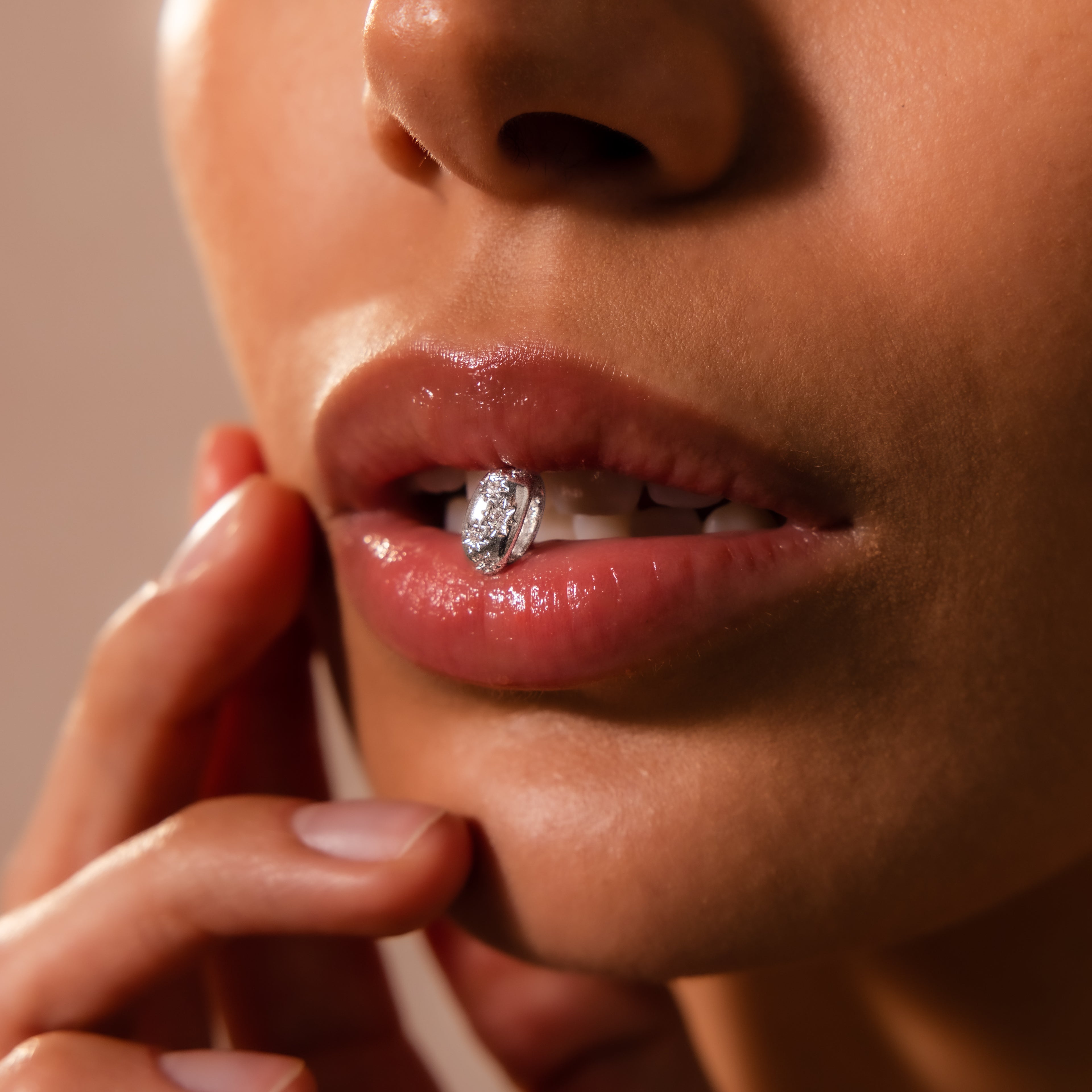 Close-up of a woman's lips holding a diamond ring between her teeth, her hand on her chin, adorned with the Sprinkle Diamond Dome Charm in Silver for an elegant touch.
