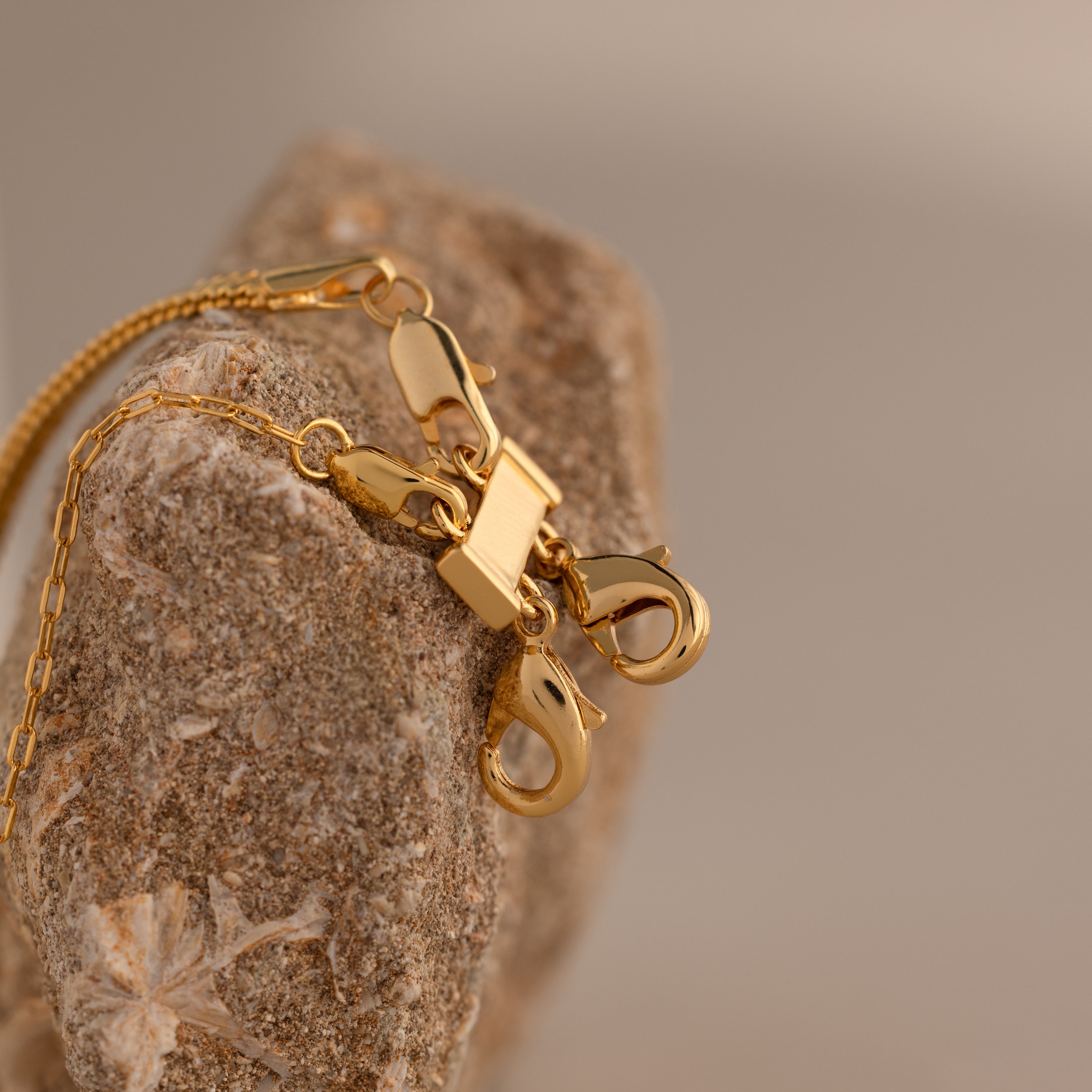 The Double Layering Clasp, designed to prevent jewelry tangles, is displayed draped over a textured rock with a neutral, softly blurred background.