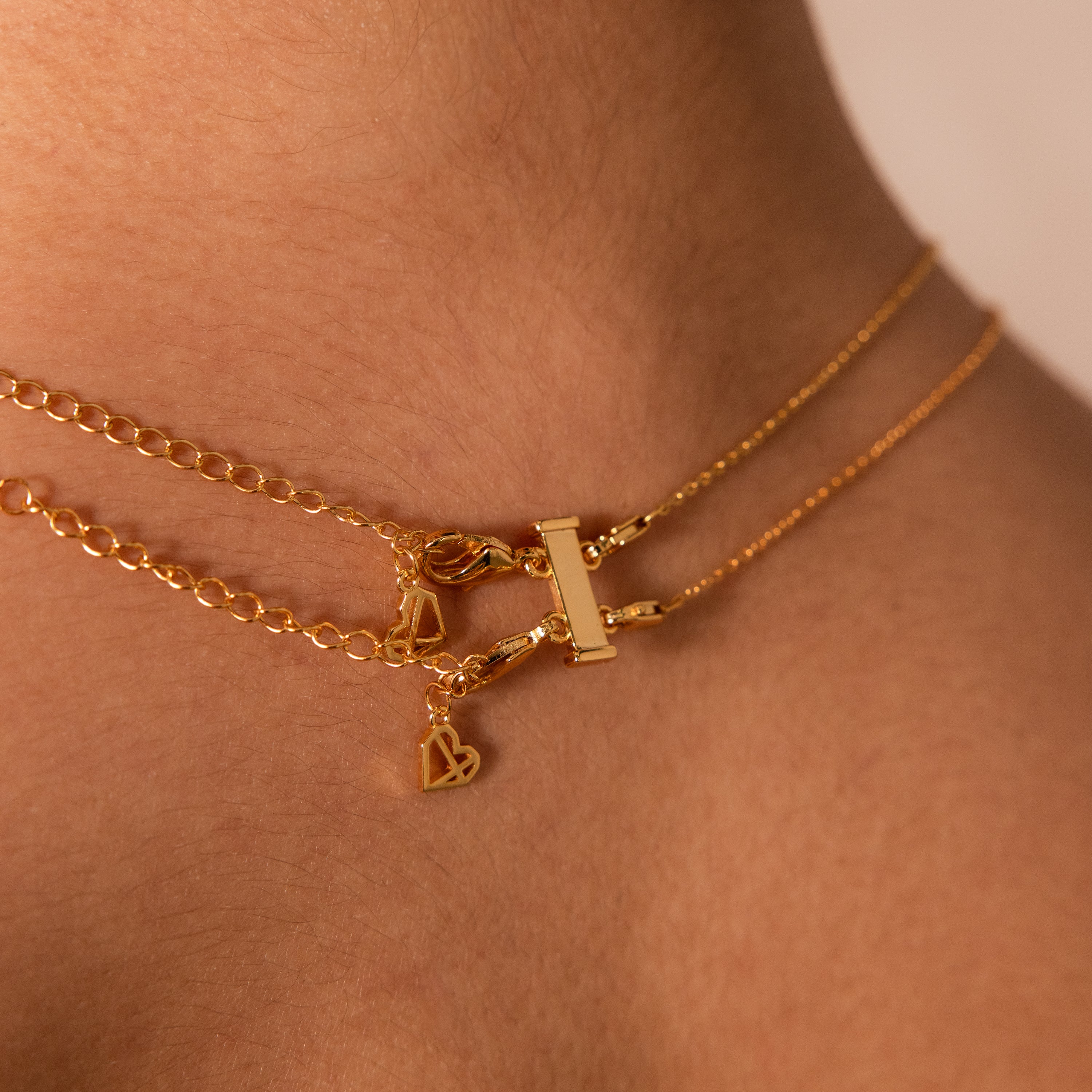Close-up of a gold layered necklace with a bar pendant and heart charm, effortlessly styled using the Double Layering Clasp for perfect necklace layering.