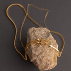 The Double Layering Clasp in 18K Gold, ideal for creating layered necklace styles, is displayed draped over a rough brown stone against a dark background.