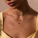 A woman wears a yellow top and layers gold and silver necklaces using the Triple Layering Clasp in 18K Gold, including a gold "shine" necklace.