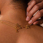 Close-up of a hand fastening a gold necklace with heart charms around someone's neck, showcasing the Triple Layering Clasp for easy necklace stacking and tangle-free wear.
