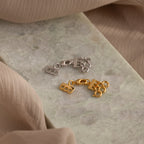 The Triple Layering Clasp in Silver keeps your necklace layers tangle-free—perfect for layering silver and gold “88” clasp charms on green marble and beige fabric accents.