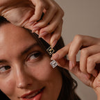 A woman holds an Onyx Hummingbird Charm in Silver near her face, smiling gently and highlighting the sentimental beauty of personalized jewelry.