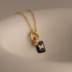 Onyx Butterfly Charm in 18K Gold: A gold necklace with a black rectangular pendant featuring a butterfly design and small sparkling stones.