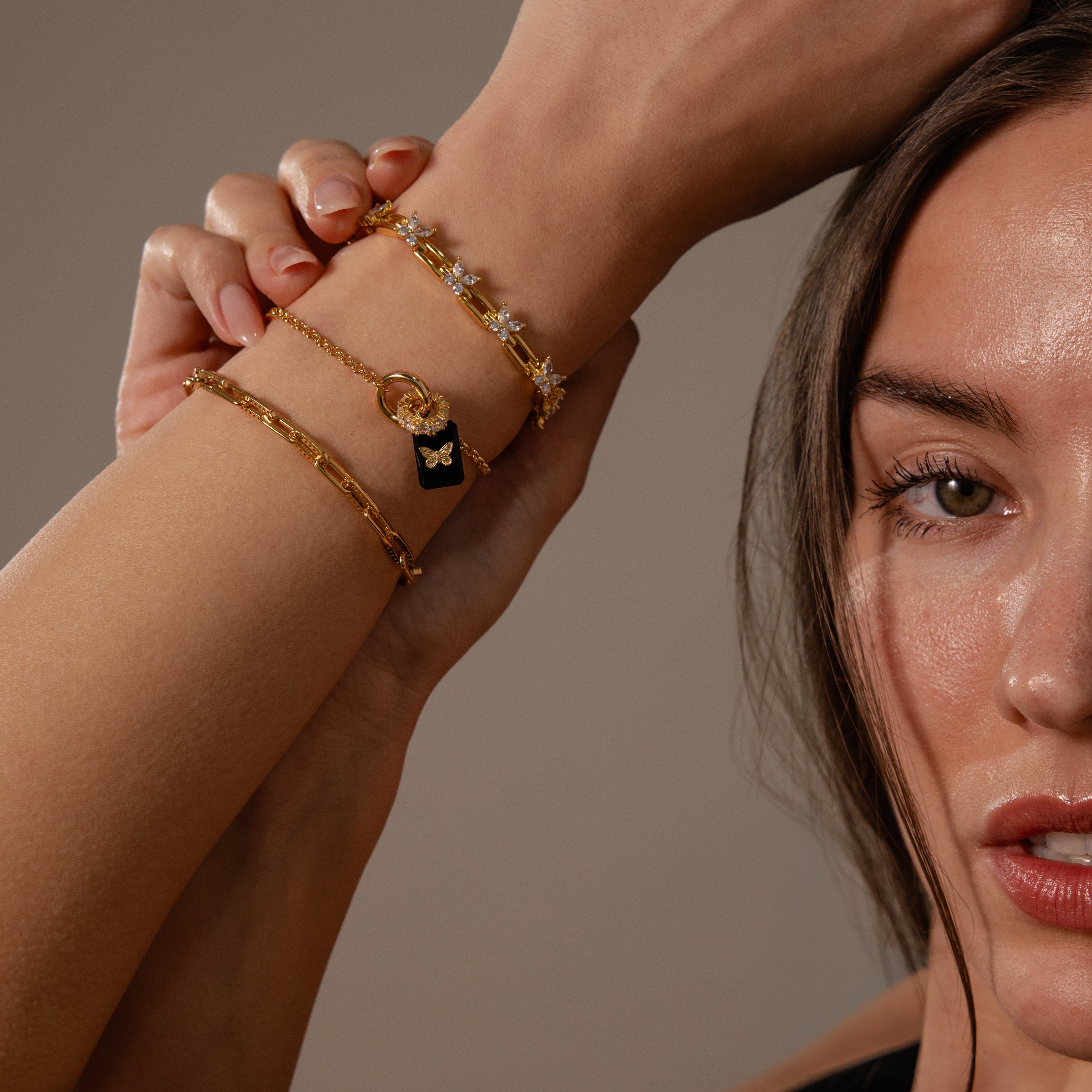 Close-up of a woman’s face and arms wearing the Onyx Butterfly Charm in 18K Gold and a crystal bracelet, highlighting elegant jewelry perfect for any occasion.