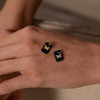 A hand showcases two Onyx Butterfly Charm in Silver rings, each black and rectangular with detailed butterfly designs, combining silver and gold tones for a unique, elegant look. No additional product description is available.