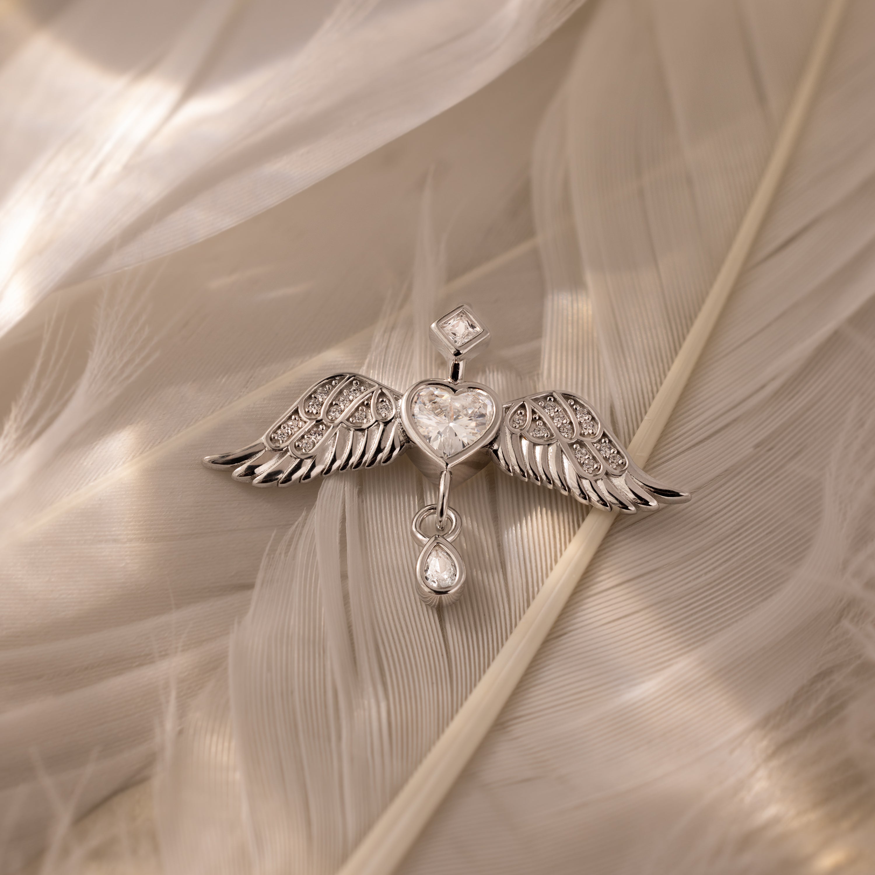 Angel Wing Charm in Silver features pavé-set wings and sparkling gemstones, beautifully displayed on soft, light feathers.