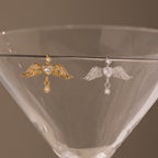 Gold and silver Angel Wing Charms with pavé diamond crystals, draped on a martini glass—ideal as protection jewelry or a sophisticated pendant.