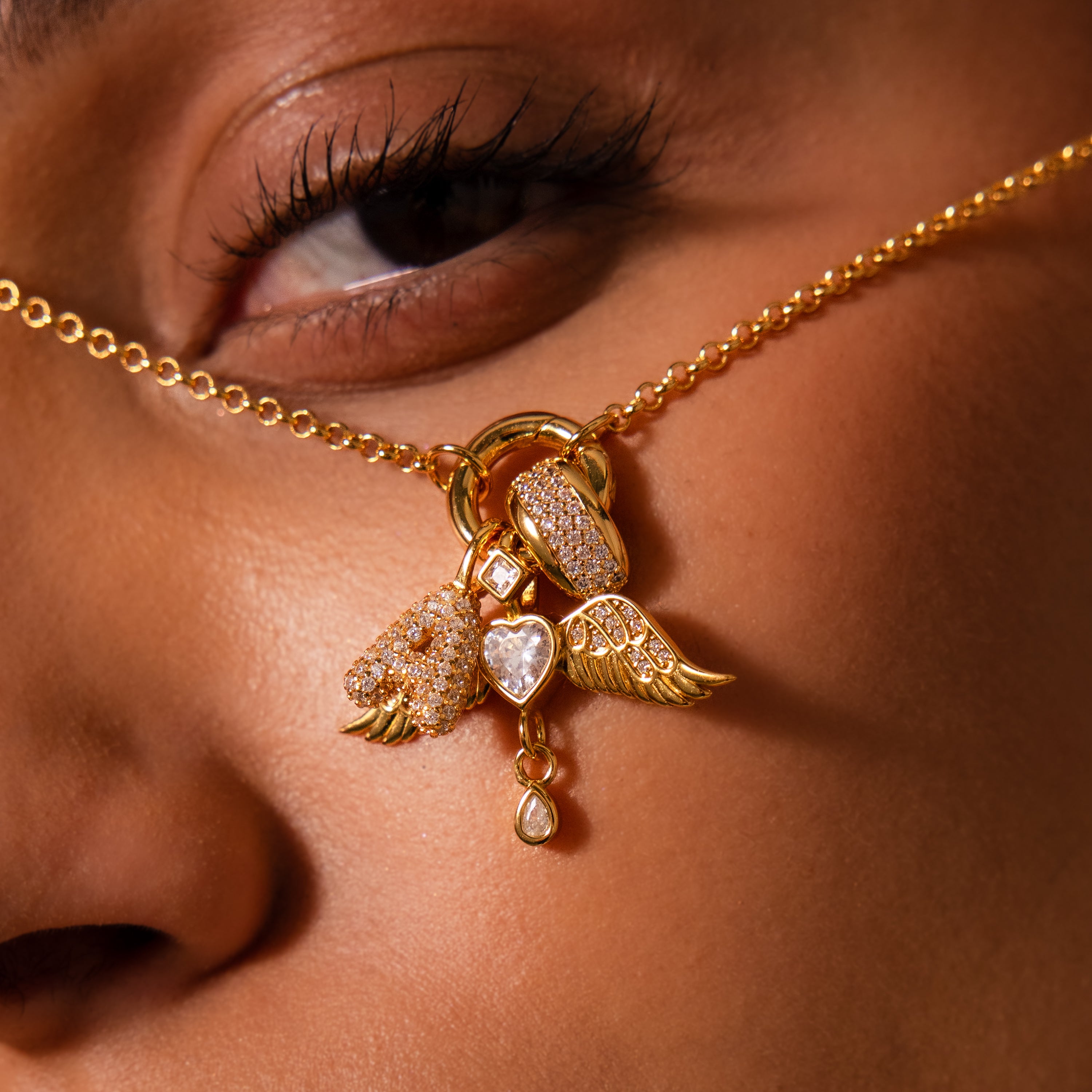 Close-up of the Angel Wing Charm in 18K Gold, featuring pavé-set wings and heart charms, held near a person's eye and nose.